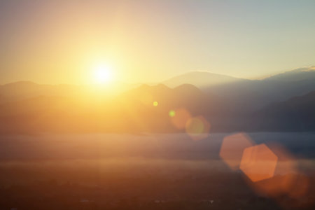 Natural fog and mountains sunlight background blurring, misty waves warm colors. Christmas background sky sunny color orange light patterns, abstract flare evening on clouds blur.の写真素材