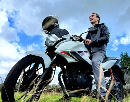an adult man of 30-45 years old sits against the sky on motobike and looks into the distance a white...