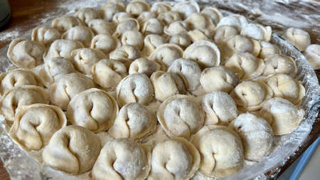grandmother for 80 years with love prepares dumplings for her grandchildren and children, she sits in the kitchen and sculpts dumplings and dumplings shakes and kneads the doughの写真素材