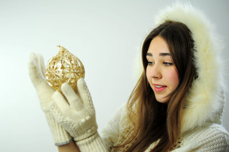 Postcard with a beautiful woman Snow Maiden young beautiful girl in mittens holds in her hands a toy that is for the Christmas tree She is wearing a hoodie with fur White gloves hold a golden ballの写真素材