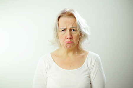 The woman pouted, she drank her lower lip and looks with sad eyes into the frame she is in a white T-shirt on a white background she has blond hairの写真素材