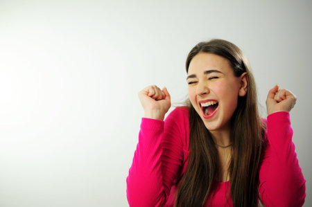 Life is wonderful Joyful lady keeps fists clenched, tilts head and exclaims in triumph, celebrates success, with blank space for your advertisement happy and cheerful smiling moving casual confidentの写真素材