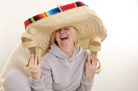 An adult woman holds beautiful high-heeled straw shoes in hands, she waves them rejoicing and dancing Sport suit mexican hat dancing Dancing mature Mexican woman in sombrero hat on white backgroundの写真素材