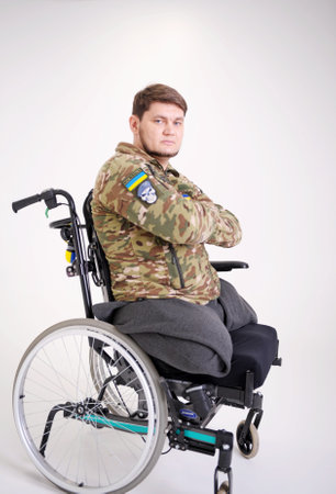 Upset young male looking at camera with sad look. He is sitting in invalid chairing wearing military uniform Handsome disabled soldier sitting in a wheelchair Veteran of war with disabilityの写真素材