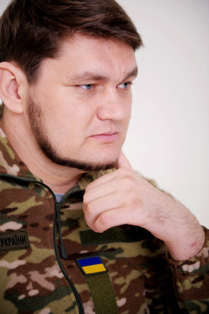 Ukrainian soldier leaned his head on hand and thought he looks down he has beautiful blue eyes beard and uniform. a lot of pain and sadness in his eyes. the war changed life. Russia attacked Ukraineの写真素材