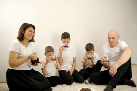 family drinking tea tea parties on the white floor black tea black chocolate chip cookies white t-shirts three sons mom and dad family coziness delicious drink weekend break breakfast white carpetの写真素材