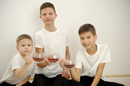 children three boys drink tea poured into transparent glass cups with double glass they look into frame on white background black pants brothers tea drinking and love for home joy friendship restの写真素材