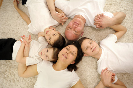 Upper view of family of four laid on carpet happy family holding on carpet with clasped hands at homeの写真素材