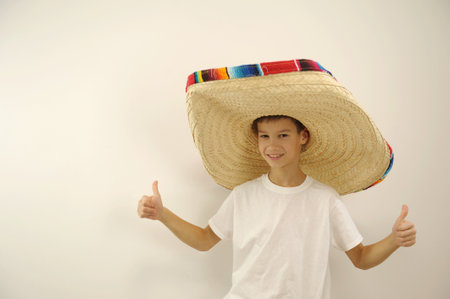 Young Mexican patriot with a ranger hat celebrating El Grito de Independencia boy in a huge mexican hat shows thumbs up on both hands class he approves something place for text on a white backgroundの写真素材