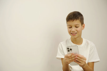 Using smartphone, looks calm. Caucasian boy portrait isolated on white studio background. Beautiful teen male model in white shirt posing. Concept of human emotions, facial expression, sales, ad.の写真素材