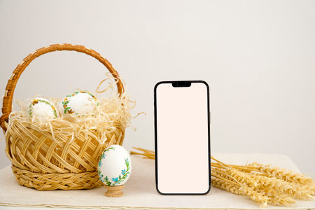 Easter holiday phone with white background basket eggs with embroidered pattern ribbon embroidery on eggshells wheat spikelets on table place for dough close-up basket to church white screenの写真素材