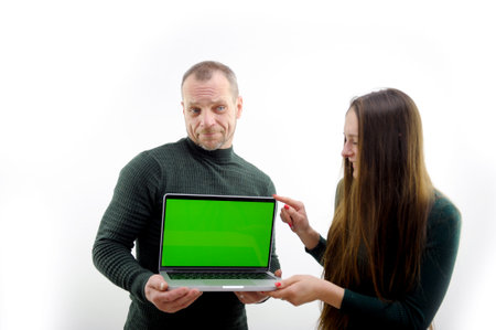 serious adult man and girl showing a laptop screen with his hand space for advertising text Green background chroma key white background white clothes clean gods make the world a better placeの写真素材