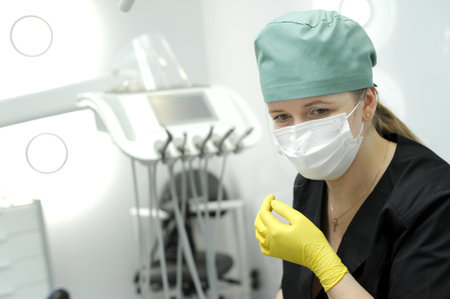 Portrait of beautiful female doctor surgeon putting on medical gloves standing in operation room....