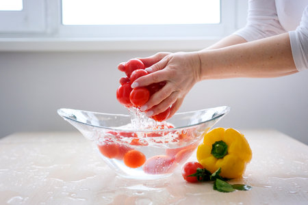 Super Slow Motion Shot of Flying Fresh Tomatoes with Water Splashing on White Background water in kitchen in morning under faucet. Preparing vegetables for making delicious veggie salad at home.の写真素材