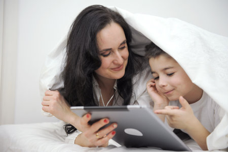 Little kid watching cartoons on tablet while sitting on the bed watching cartoons with him. Bedroom...