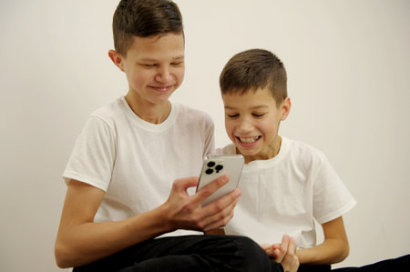 Shocked kids using modern smartphone with surprised emotions and eyes wide open while sitting at the break at the classroom at the school. Children, science and education conceptの写真素材