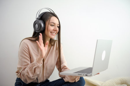 Smiling young woman wearing headphones lying on bed with laptop, teenage student studying online at...