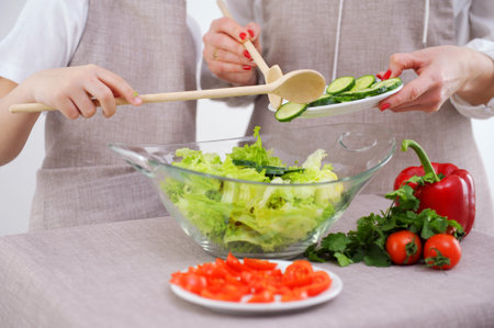 mother and child preparing vegetable salad close-up boys hands help mother to add cucumbers glass plate Professional female cook adding fresh cucumber slices in glass bowl with saladの写真素材