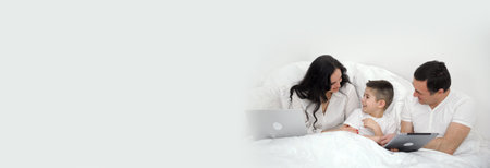 banner space for text family in bed communication tablet laptop family comfort white beds advertising bed linen gadgets leisure travel travel cozy hotels white clothes black hair mom dad and sonの写真素材