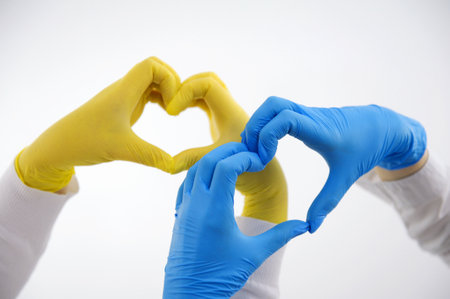 the hands of two nurses make heart in the air on white background blue and yellow latex gloves...