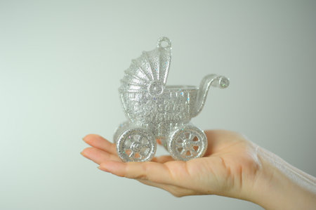 On a white background in the studio on the palm of a woman lies Silver baby carriage Christmas tree toy Space for invitation text birth of child Invitation to christening or meeting from hospitalの写真素材
