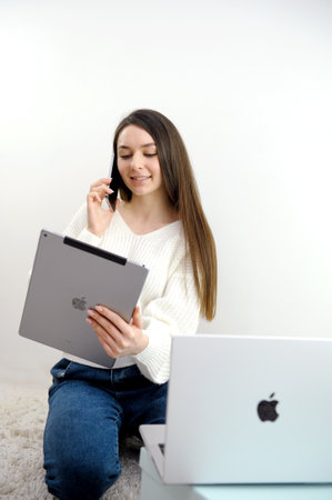 new technologies Apple MacBook 14 pro phone iPhone 13 pro Max and iPad on a white background the girl uses all the latest technologies talking on the phone smiling holding a tablet looking at a laptopのeditorial素材
