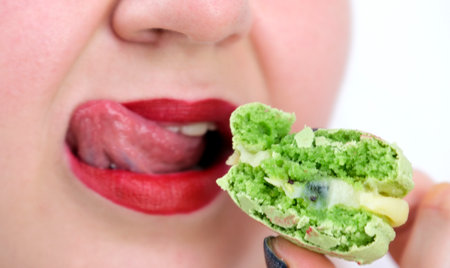 Beautiful fashion model girl with red lips bites colorful macaroons. Closeup. Happy woman eating french macaroon. Female holds colorful macaroon. French dessert. Sweets. Beautiful woman bite macaroon.の写真素材