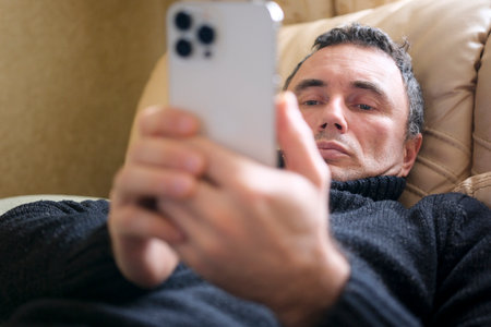 business man lie on the bed. Holding and looking at the smart phone in his hand. Concept of Mobile...