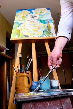 Young craftswoman in apron paints clay vase with paintbrush after baking and handmade shaping in studio. Woman enjoys painting earthenware vase in workroom for handmade pottery shop closeupの写真素材