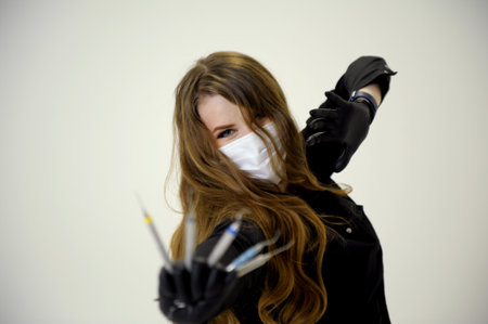 Beautiful woman dentist in a black suit with a white mask with flowing hair holds in her hands scaler and curette Hand stretched forward selective focus bright photo of gorgeous womanの写真素材