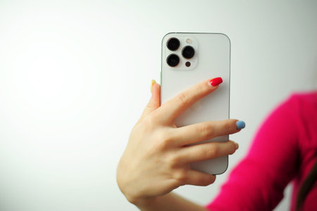 iPhone apple 13 mini in female hands,smartphone phone isolated on white hand with multi-colored manicure white background pink jacket girlsのeditorial素材