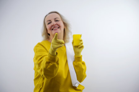 woman with yellow sweater points finger at you while smiling blonde woman pointing at camera with a satisfied, confident, friendly smile, choosing you against flat color wallの写真素材