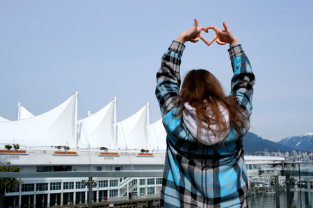 girl teenager woman stands with her back to the camera makes heart travel with her hands Canada Place, Vancouver, British Columbia, Canada Radiance of the Seas Cruise Ship Docked at Canada Place.の写真素材