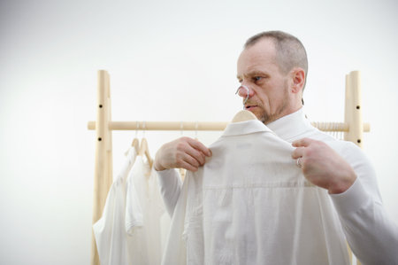 man isolated in front of white background holding two shirts The man cant decide which shirt to wear. Not being able to decide on the choice of clothes.の写真素材