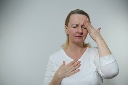 Upset stressed older woman holds head with hands sit on sofa near laptop, suffers from strong severe...