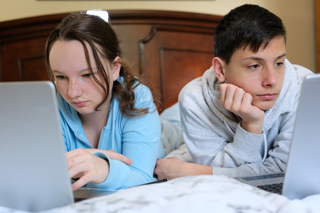 boys a girl lie on their stomachs everyone looks at their computer online learning brother and sister one room for two little space family life alone in a one-room apartment defend the boundariesの写真素材