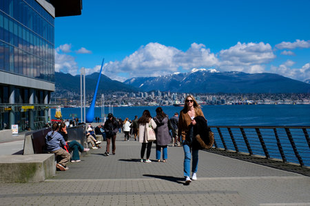 you can see the statue of a drop from the Pacific Ocean restaurants cafes glass office building mountains white clouds people walking along the embankment seagull flying in the sky port Canada Placeのeditorial素材