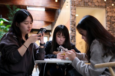 life on smartphones three young Asian women sit in a cafe at a table each with their gadget phone in social networks internet wi-fi spend time together at the same time separately Life in a big cityのeditorial素材