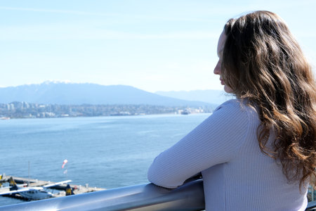 young girl stands at railing of the balcony and looks into the distance at the mountains and ships in the center of vancouver wear sunglasses straighten her hair lilac color in clothes vacation tripの写真素材