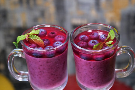 taking out a teaspoon from a glass cup delicious blueberry dessert with mint and cream jelly cooking close-up food human hand on a dark backgroundの写真素材