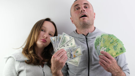 father and daughter a lot of money in their hands joy success dollars euro 100 dollar bill wave money like a fan look into the frame make faces confidence success big win purchase giftの写真素材