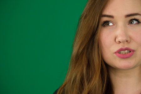 dissatisfied expression on the face of a young woman size Plus, her mouth is slightly open, she tells, she solves the problem, close-ups on a green background, her face looks to the sideの写真素材