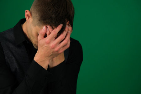 emotions of a handsome man guy on a green background chromakey close-up dark hair young man European teenager boy dressed in a black T-shirt is worried and holds his headの写真素材