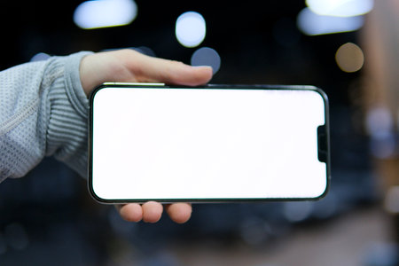 Great Mobile Offer. Lady Pointing Finger At Smartphone Emotionally Reacting To New App, phone with a white screen in hands in the gym close-up gray clothes with long sleeves advertising space for textの写真素材