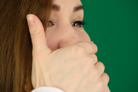 Surprised girl covering her mouth and looking at camera isolated over green backgroundの写真素材