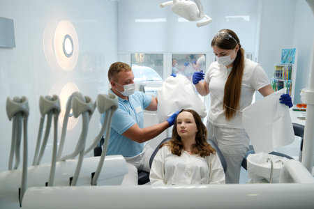 Portrait of smiling little girl in dental chair with nurse preparing her for teeth check up, copy spaceの写真素材