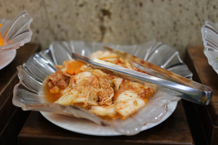 Putting homemade kimchi, Korean heritage dish, into a small bowl with wooden serving tongs.の写真素材