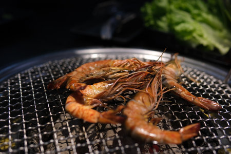 Grilled skewer shrimps and fresh vegetables served on black stony plate on wooden tableの写真素材