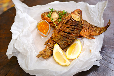 Fried fish lemons Fried whole fish with tomato and onion salad, on black background