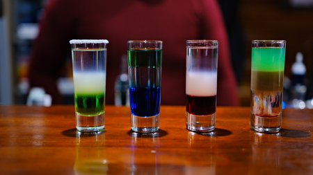 shot glasses filled with vibrant and colorful drinks sits on a sleek bar counter. The various hues reflect light and create an energetic atmosphere, perfect for a night out.の写真素材